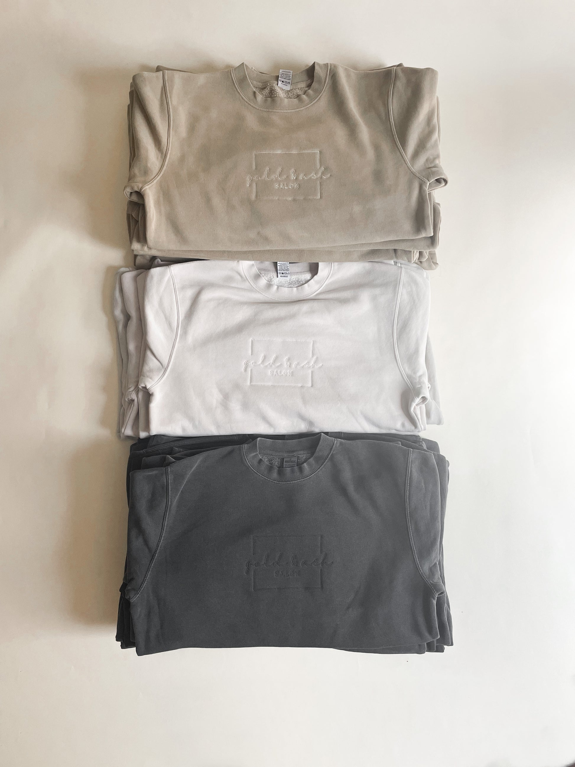 Stack of sweatshirts with custom embroidered logo for custom salon merch
